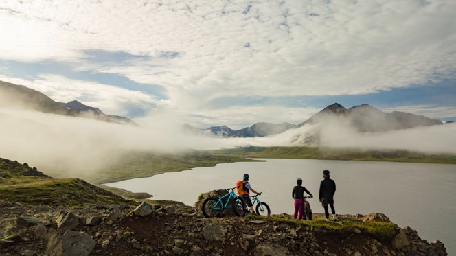 Three bikers overlooking a lake surrounded by mountains in Iceland.